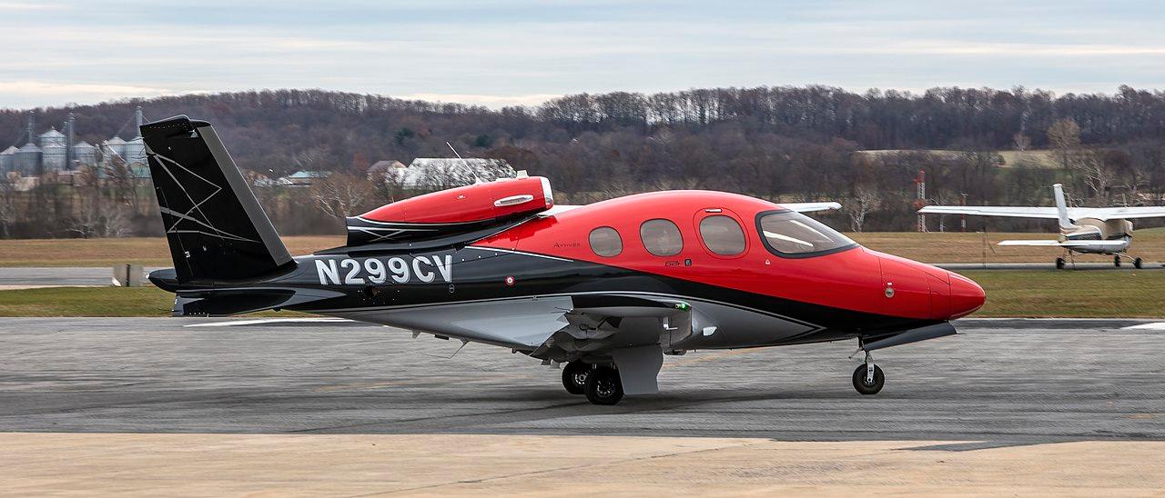 A red and black Cirrus Vision jet with tail number N299CV parked at an airport.