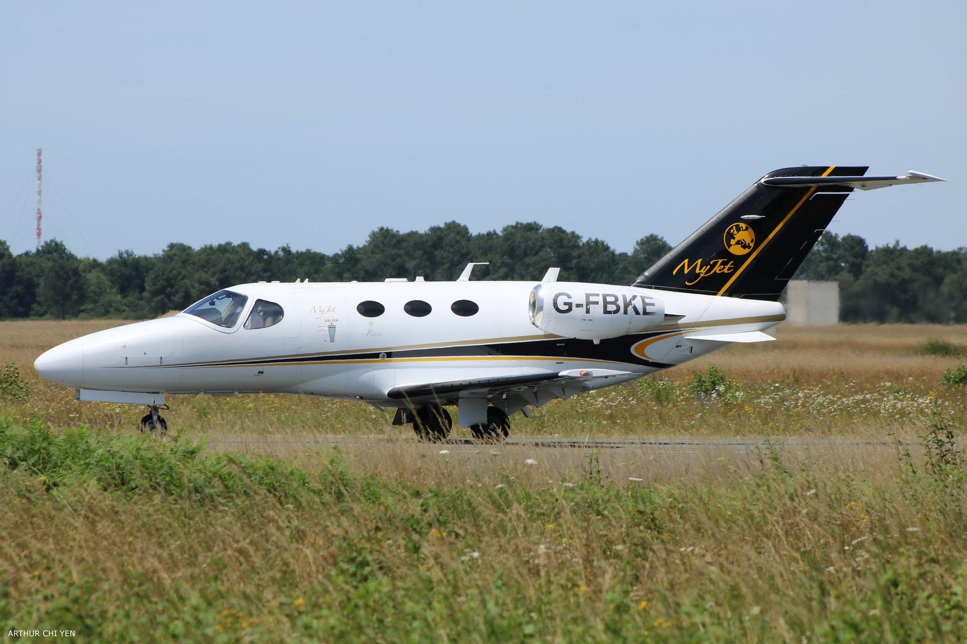 A white Cessna Citation Mustang on a taxiway behind grassy field.