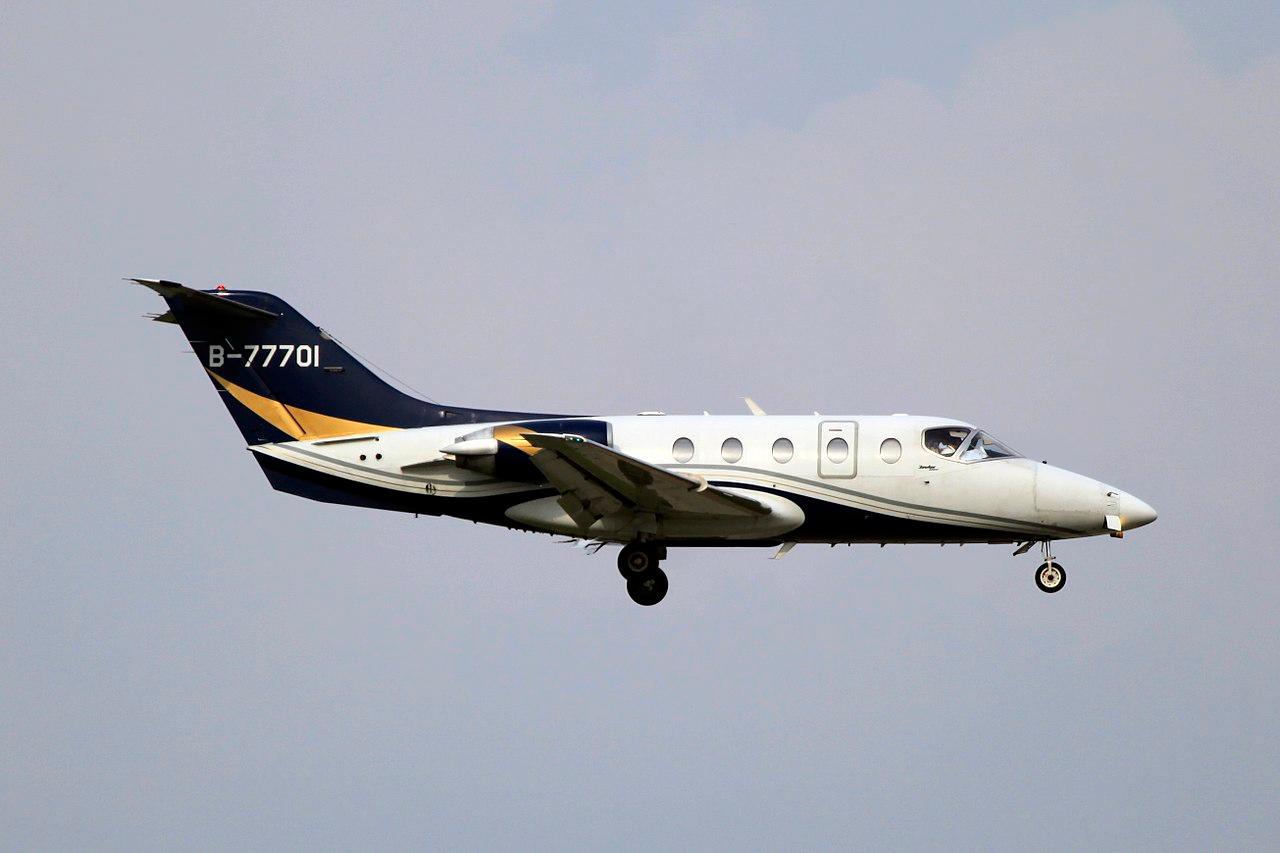 A white Hawker 400XP with black and gold accents descending with its landing gear down.