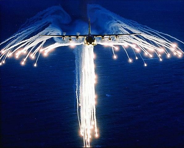 A C-130 deploying bright flares at night, resembling the shape of angel wings.
