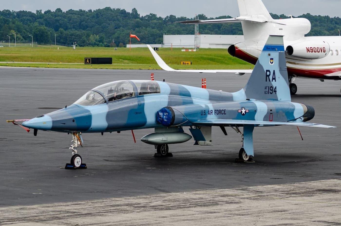 A T-38C Talon painted in a blue camo parked at an airport.